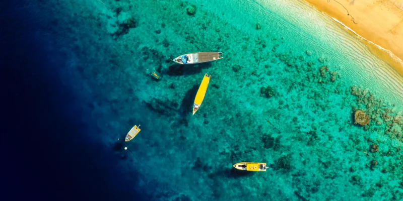 Vue aérienne de bateaux dans des eaux côtières turquoise près d’une plage de sable